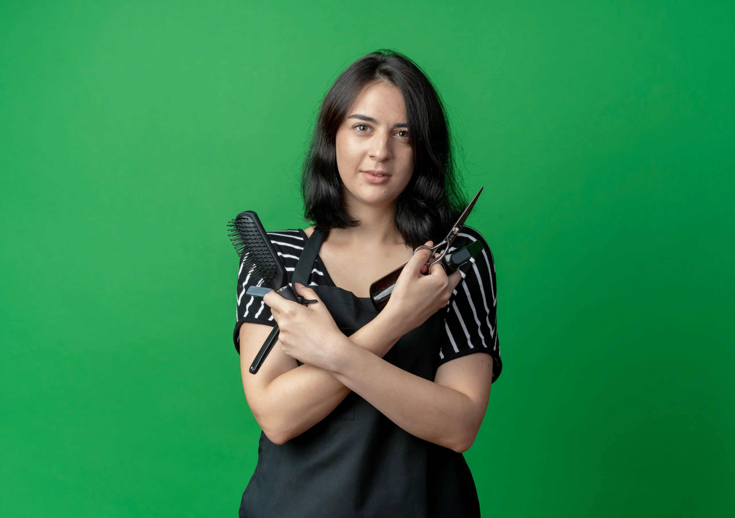 young beautiful female hairdresser apron holding scissors spray brush with confident smile crossing hands green scaled 1